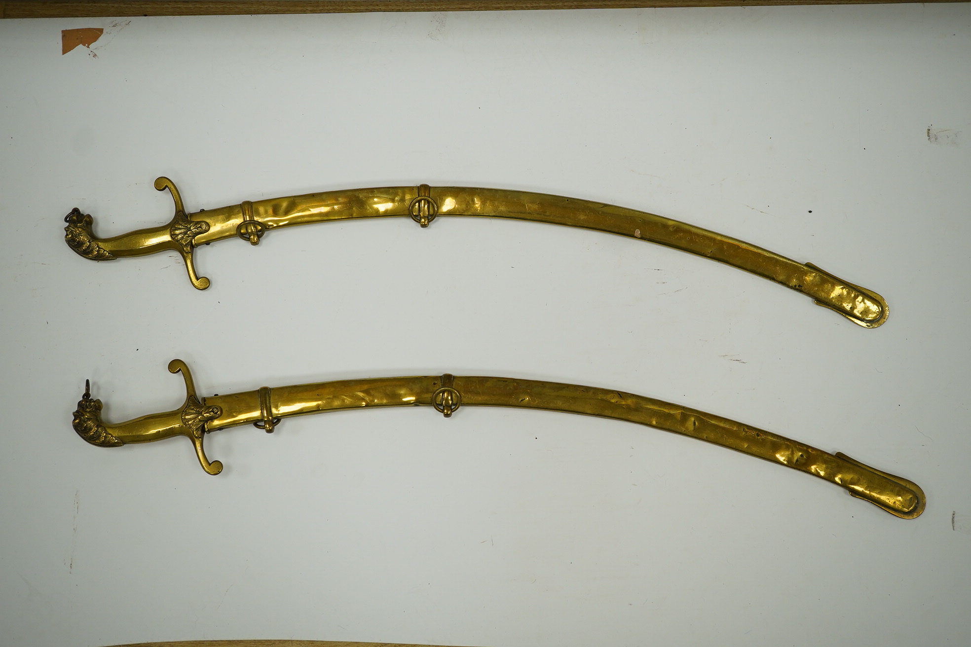 A pair of Victorian bandsman’s swords of Shamshir type, curved single edge blades, cast brass hilts with lions head pommels, in their brass scabbards. Condition - good, some dents to scabbards.